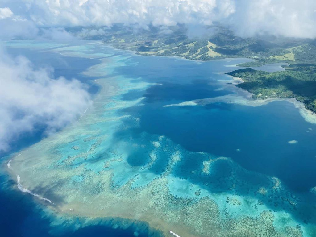 Aerial view of tropical coral reefs with turquoise ocean and islands with lush rainforests
