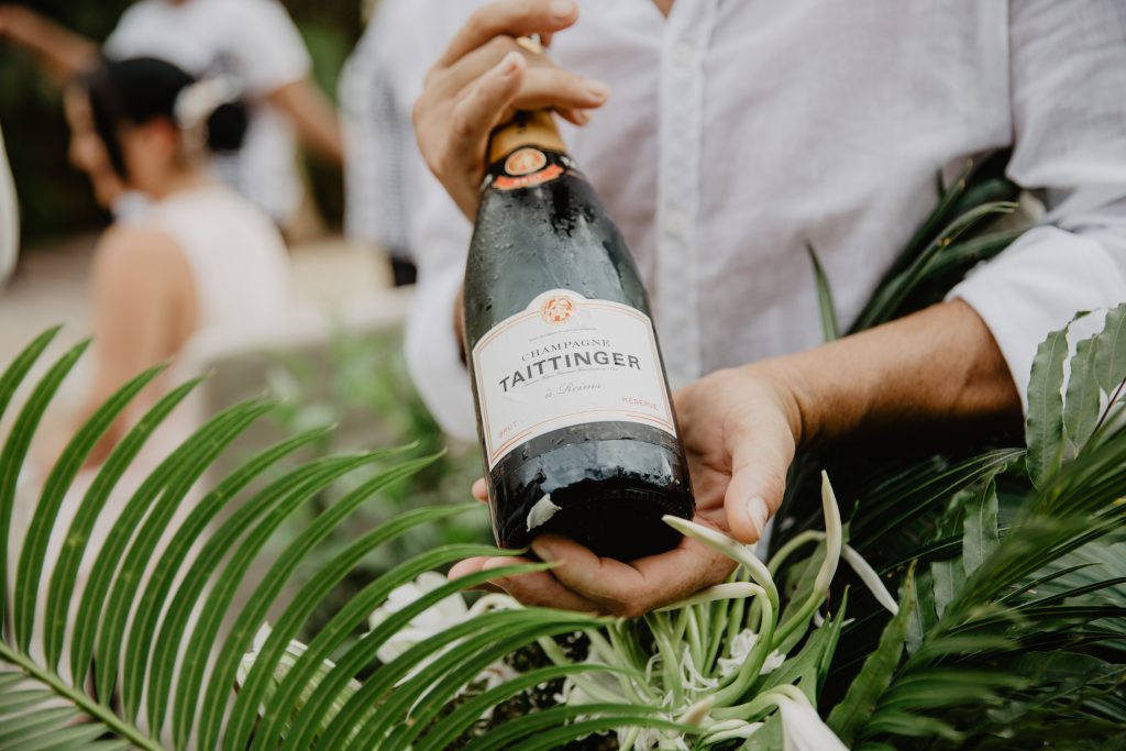 A bottle of Taittinger champagne presented by a waiter with green palm fronds in the ice bucket.