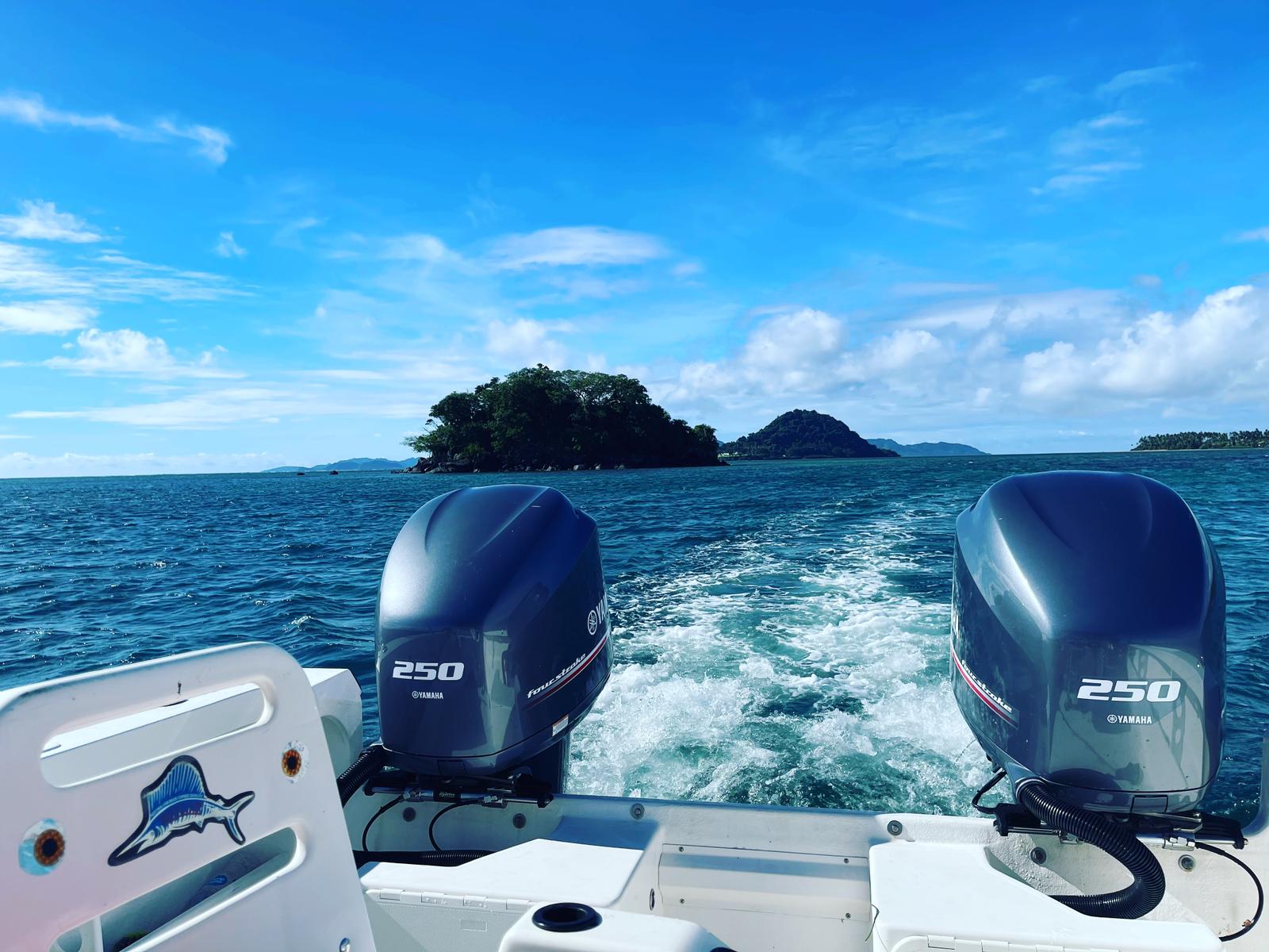 Looking out back of fishing boat to island with clear blue sky, Fiji